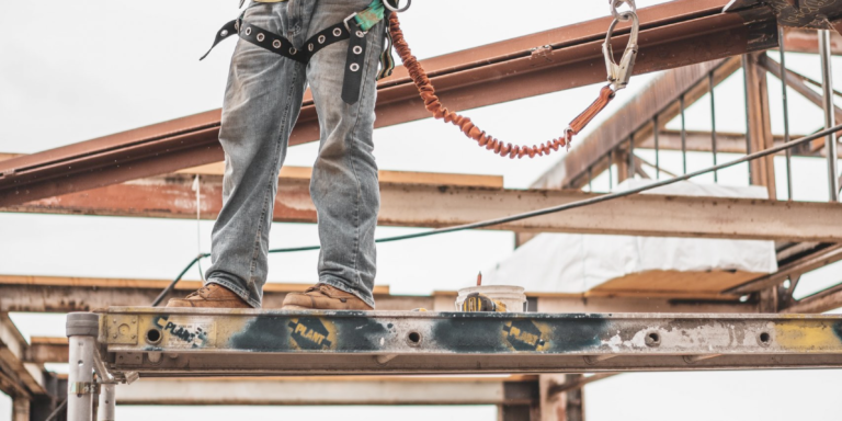 Photo of construction worker wearing a safety harness standing on steel structure